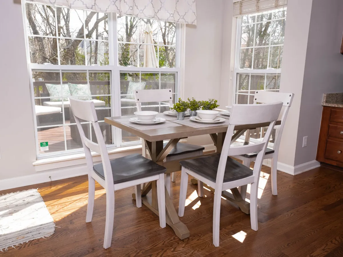 A spacious dining area with an extra-long table and several chairs, surrounded by windows and decorated with plants. Natural light streams in, creating a welcoming environment ideal for group meals or celebrations.