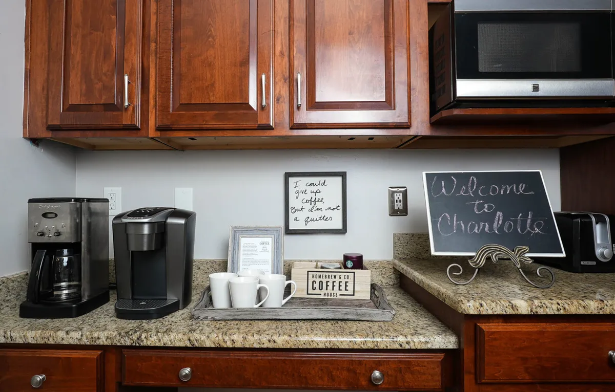 A cozy nook featuring a coffee maker, tea cups, a welcome sign, and a quote sign, inviting guests to brew their favorite drinks and gather for conversation. The scene radiates hospitality and warmth.