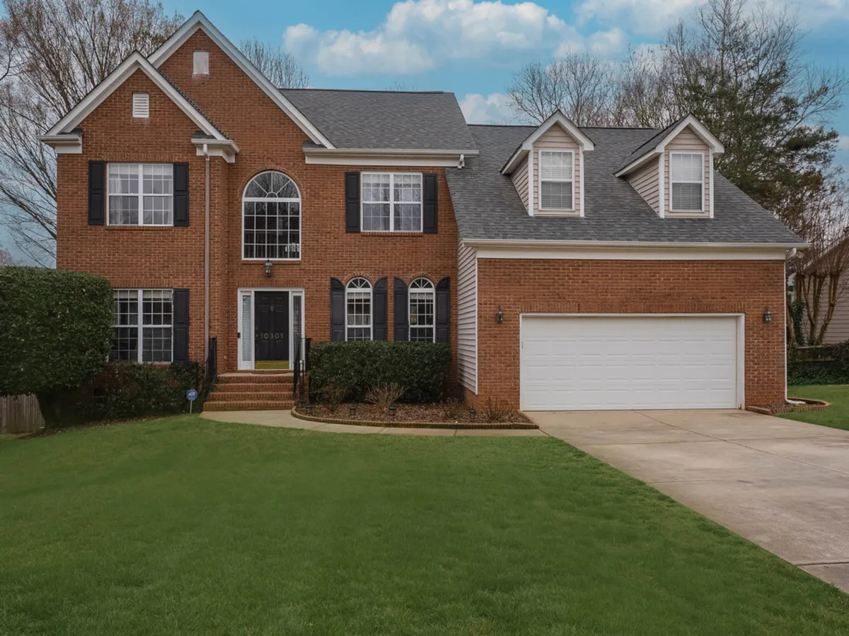 A wide view of a large brick home with an arched entryway, manicured lawn, double garage door, and inviting front porch. The house exudes a welcoming, family-oriented atmosphere, perfect for gatherings and outdoor activities.