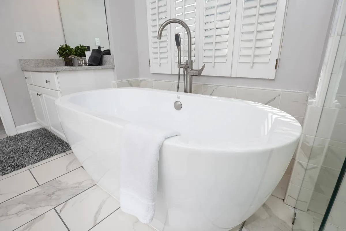 A beautiful bathroom with a freestanding bathtub, modern faucet, decorative plants, and a mirror. The room exudes spa-like tranquility, inviting guests to relax and enjoy self-care routines after a busy day.