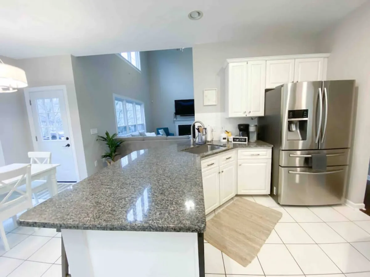 A bright, functional kitchen with granite countertops, stainless steel appliances, white cabinetry, and large windows that invite natural light. The open layout and kitchen island provide ample space for cooking and gathering.