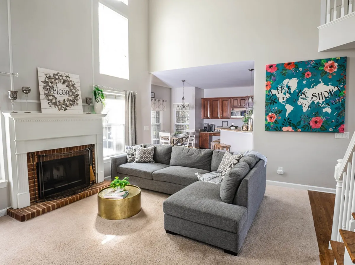 A warm and inviting combined living and dining area anchored by a fireplace, with a comfortable sofa, colorful wall art, and a visible dining area in the background. The space exudes coziness and is clearly designed for family gatherings and entertaining guests.